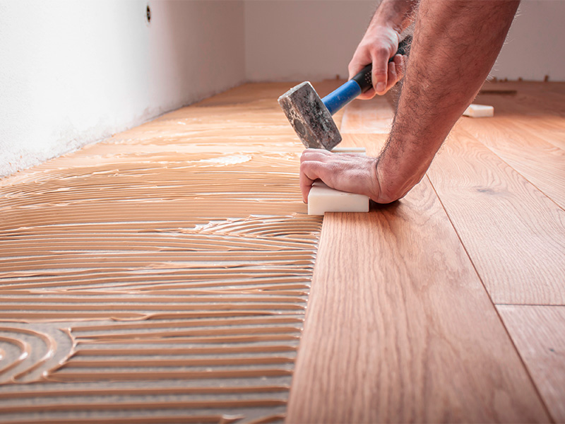 Handwerker verlegt Parkettboden, trägt Kleber auf Estrich auf und schlägt Dielen für Bodenbelag im Kreis Ahrweiler
