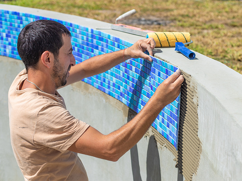 Handwerker verlegt Mosaik Wandfliesen in einem Schwimmbad – präzise Ausführung beim Wandfliesen verlegen.