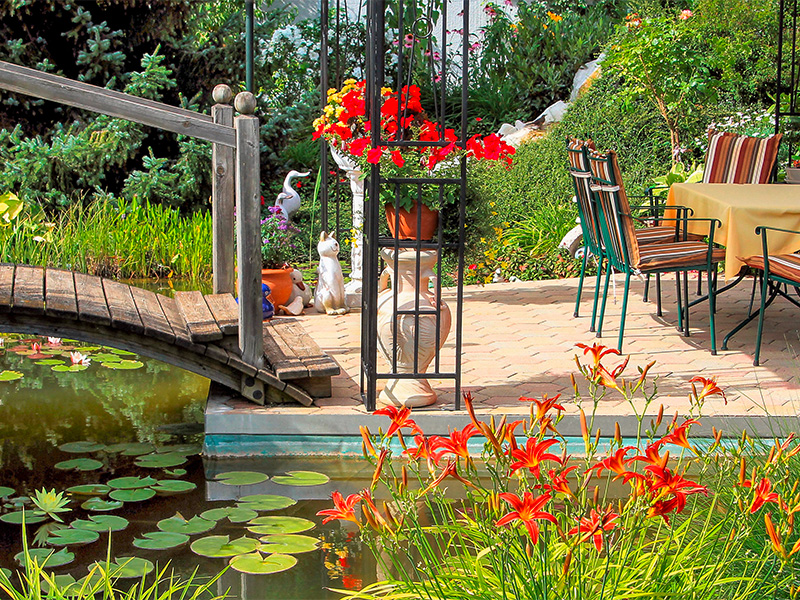 Gartenbereich mit kleiner Brücke über einen Gartenteich, Bepflanzung und Sitzplatz als Beispiel für Gartenbau in Remagen