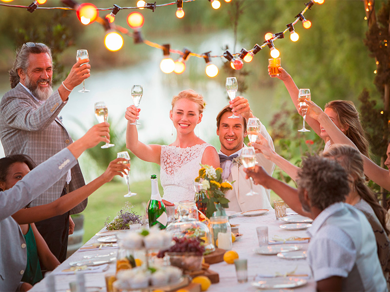 Junges Paar stößt mit Gästen auf Hochzeit im Garten an – professioneller Getränkeservice im Kreis Ahrweiler.