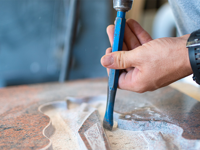 Steinmetz bearbeitet eine Grabsteingravur von Hand in der Werkstatt und sorgt für präzise Details sowie eine hochwertige Ausführung.