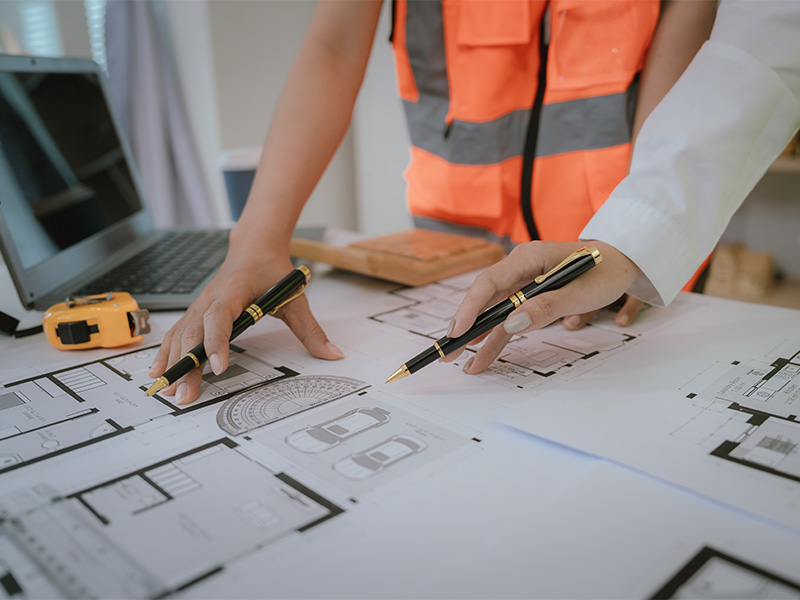 Architekt und Sachverständiger prüfen ausgedruckten Bauplan auf Tisch – Symbol für professionelle Bewertung eines Einfamilienhauses