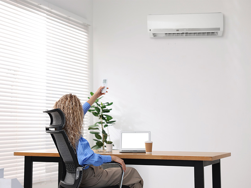 Frau steuert moderne Klimaanlage per Fernbedienung im Büro, Symbol für effiziente Kälte- und Klimatechnik im Kreis Ahrweiler.