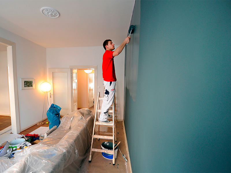 Malergeselle führt Malerarbeiten in einer Altbauwohnung aus und bearbeitet eine Wand im Rahmen der Renovierung