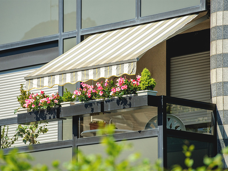 Balkon mit geöffneter Balkonmarkise als Sonnenschutz und blühenden Pflanzen an einem Sommertag.