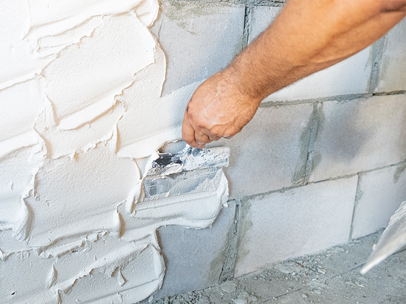 Handwerker trägt Putz mit Spachtel auf Innenwand auf und glättet Oberfläche bei Verputzarbeiten im Neubau oder Renovierungsprojekt