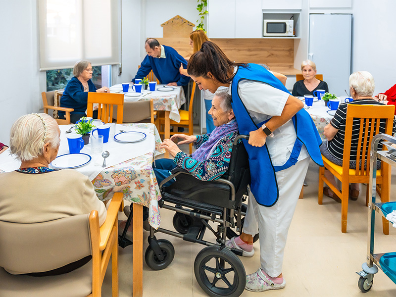 Pflegekraft unterstützt Seniorinnen und Senioren beim gemeinsamen Essen in der Tagespflege in Bad Neuenahr.