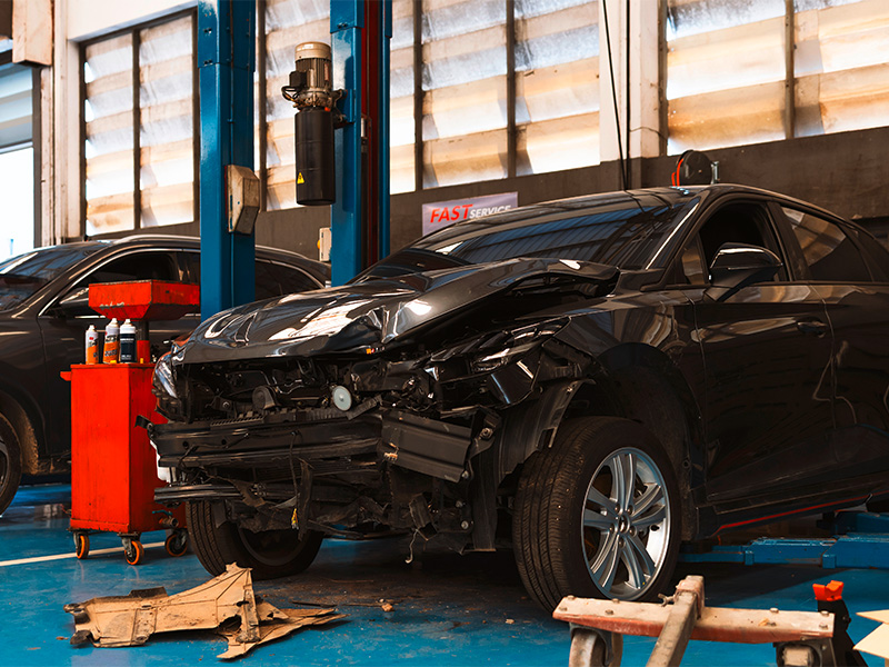 Beschädigtes schwarzes Auto mit eingedrückter Motorhaube in einer Werkstatt für Unfallreparatur in Sinzig.