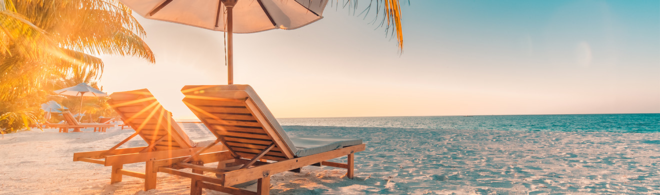 Paar genießt den Sonnenuntergang am Strand mit Liegestühlen, Sonnenschirm und Palmen – perfekte Inspiration für Urlaub buchen in Sinzig.